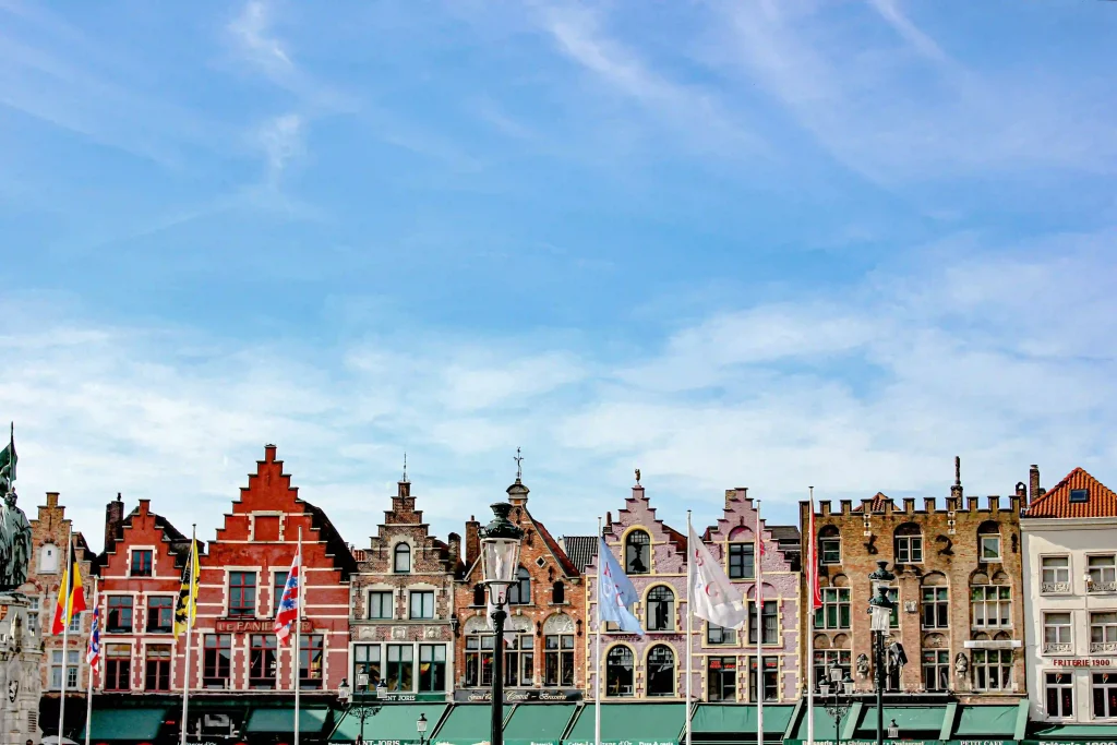Historic stepped gables and colorful buildings on the Market Square in Bruges under a blue sky.